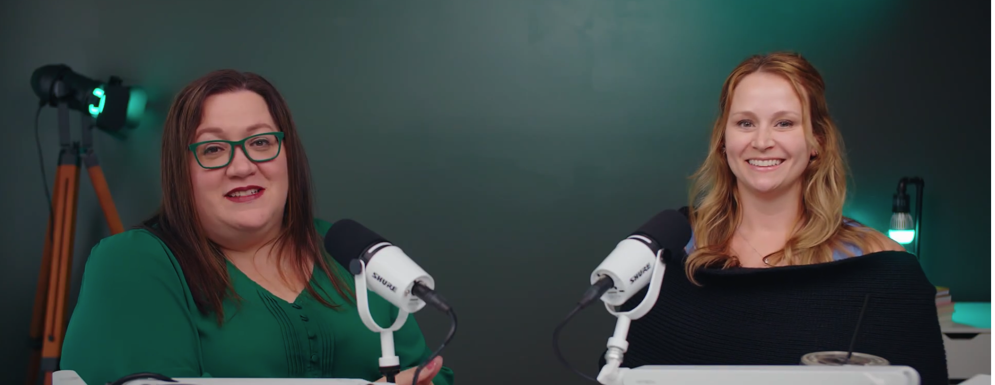 Amy K. Nunn and a podcast guest smiling at their microphones during a recording.